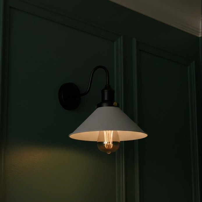 Wall-mounted lamp with a white shade and exposed bulb against a dark green wall.