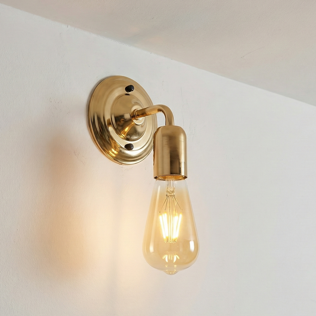 Gold wall sconce with a lit bulb on a white wall
