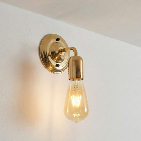 Gold wall sconce with a lit bulb on a white wall