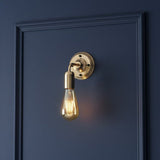 Gold wall sconce with a lit bulb on a dark blue wall