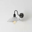Wall-mounted light fixture with white shade and black metal arm on a light gray background