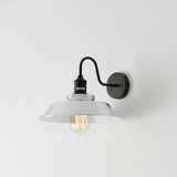 Wall-mounted light fixture with white shade and black metal arm on a light gray background