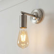 Wall-mounted light fixture with a clear bulb on a white wall.