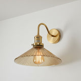 Gold wall-mounted lamp with amber glass shade on a white wall