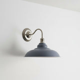 Wall-mounted light fixture with a slate blue shade and brass arm on a white background