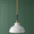 White pendant light with a gold cord against a green paneled wall