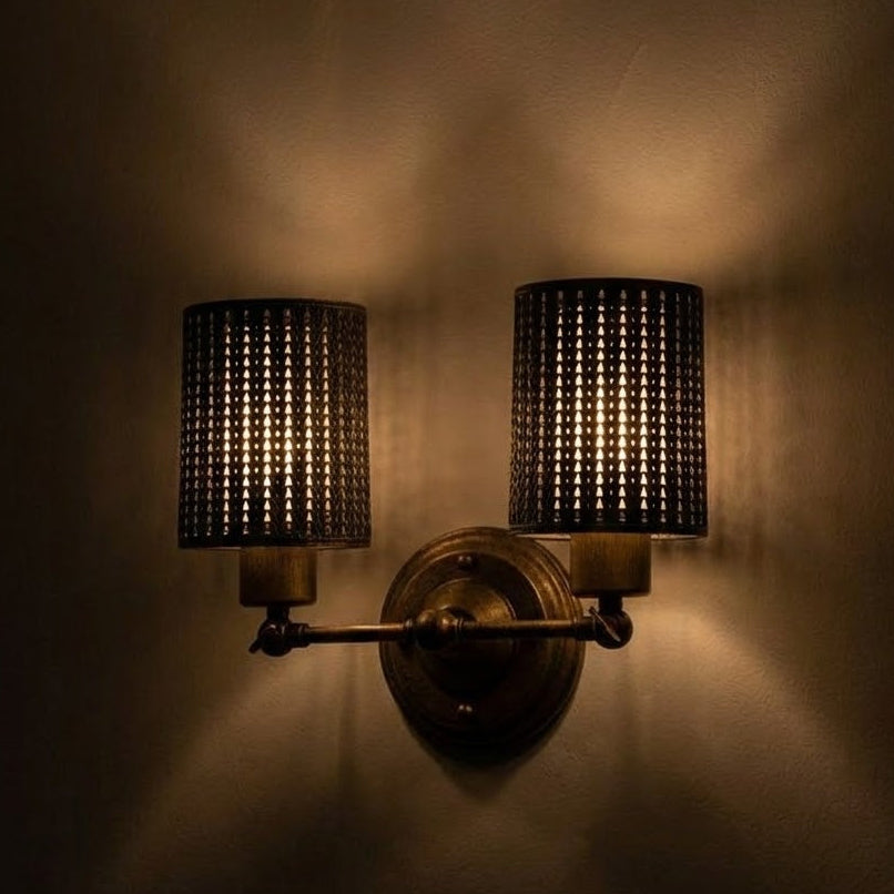 Wall-mounted light fixture with two lampshades on a dark wall.