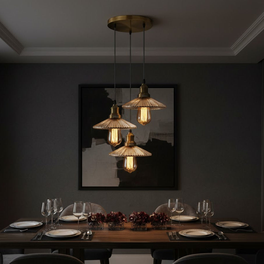 3 pendant light over Dining table set with plates, glasses, and a framed picture on a dark wall.