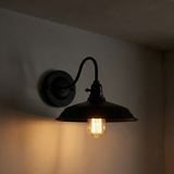 Black wall-mounted lamp with a lit bulb on a dark background