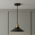 Black pendant light with brass fitting hanging against a gray wall.