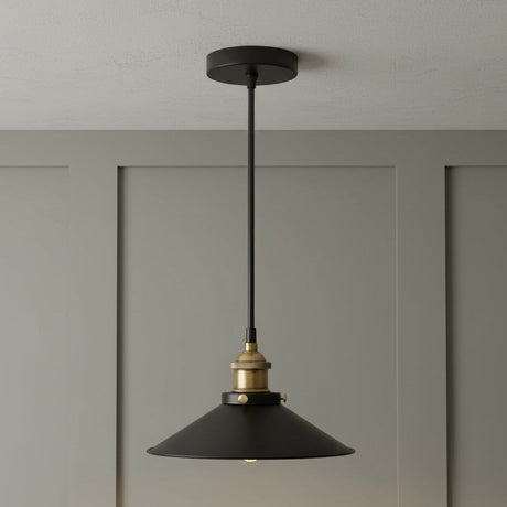 Black pendant light with brass fitting hanging against a gray wall.