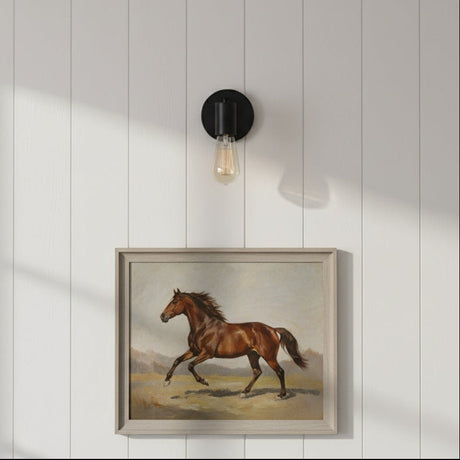 Framed painting of a horse on a white paneled wall with a wall light fixture.