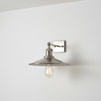 Wall-mounted light fixture with a chrome shade on a white wall