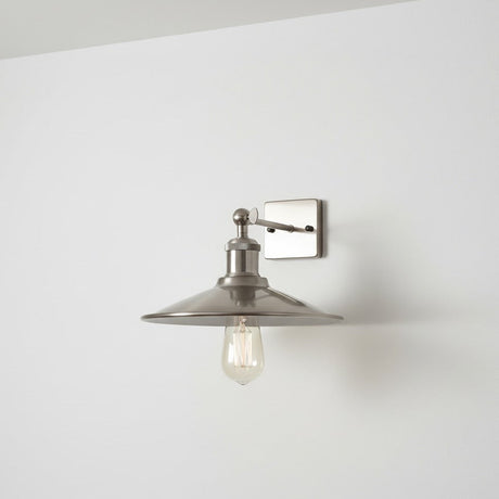 Wall-mounted light fixture with a chrome shade on a white wall