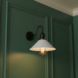 Wall-mounted light fixture with a white shade on a green wall.